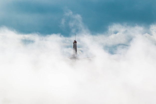 Wide shot of a lighthouse covered in white clouds in a blue sky