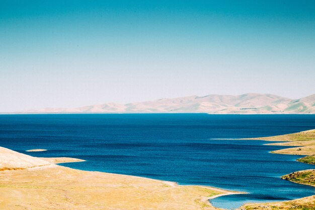 Wide shot of an ocean with sandy seashore of white mountains under a clear sky