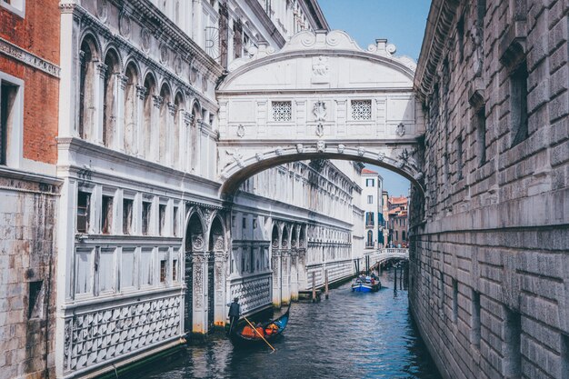 Wide shot of a person rowing a gondola on a river under The Bridge of Sighs in Venice, Italy