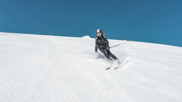 Wide shot of a skier skiing on a snowy surface wearing skiing outfit and helmet