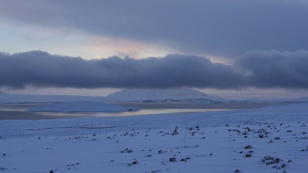 Wide shot of a snowy shore near frozen water under a cloudy sky