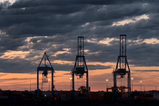 Wide shot of three towers in a port during sunset on a cloudy day