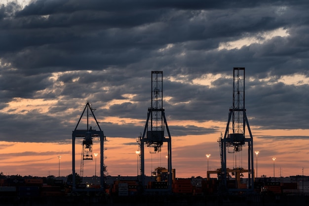 Wide shot of three towers in a port during sunset on a cloudy day