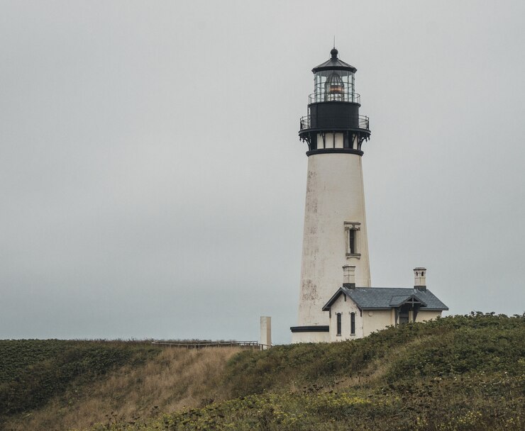 Free Photo wide shot of a white and black lighthouse near a house on the top of a hill