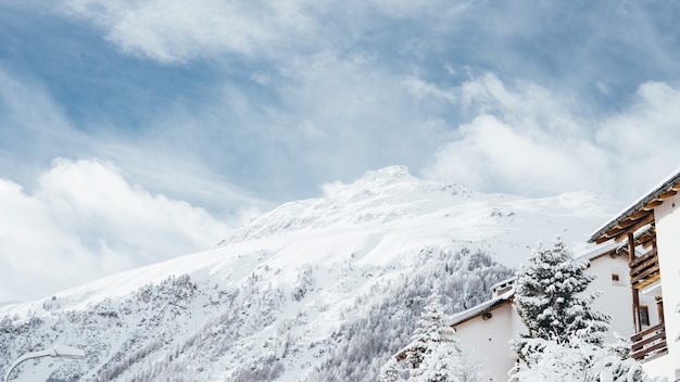 Wide shot of a white and brown house near trees and a mountain covered in snow