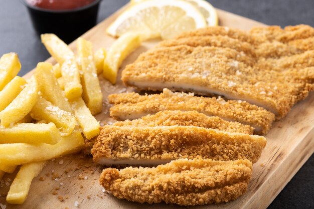 Wiener schnitzel with fried potatoes on black background