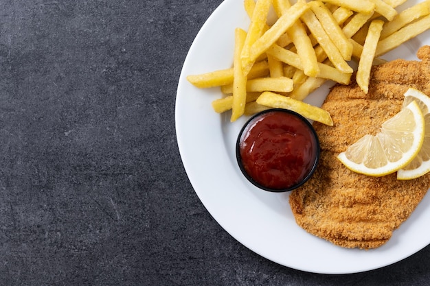 Wiener schnitzel with fried potatoes on black slate surface