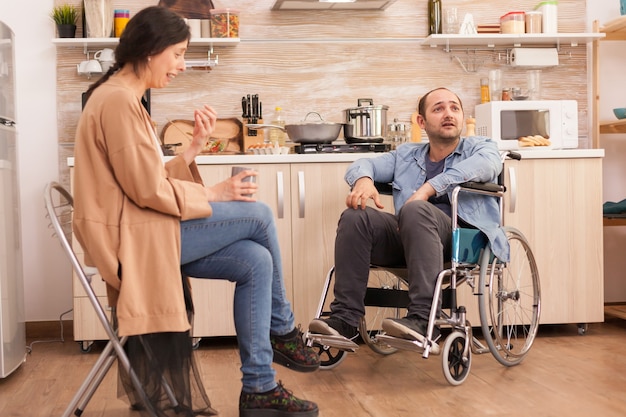 車椅子の障害者の夫との意見の相違のために泣いている妻。カップルは台所で論争します。事故後に統合した歩行障害のある障害者麻痺障害者。 Premium写真