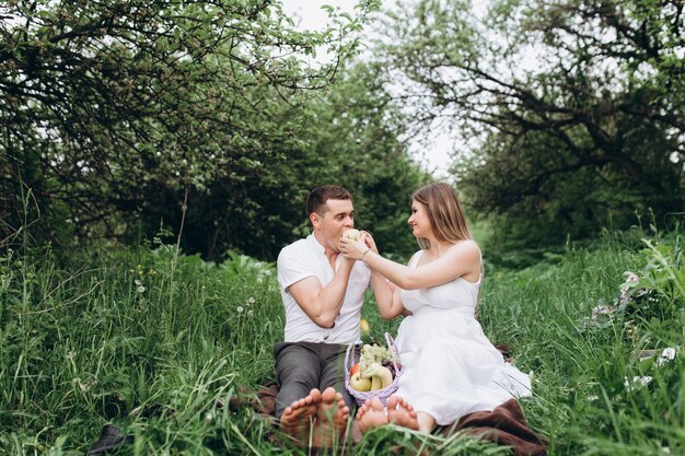 The wife and husband sittting on the plaid with fruits