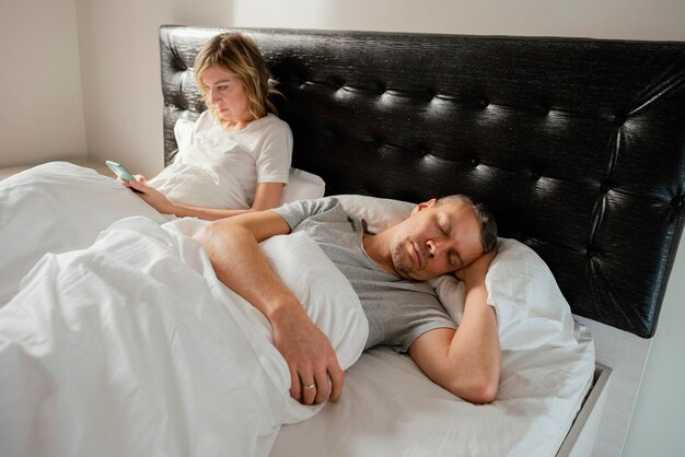 Free photo wife using mobile while husband is asleep