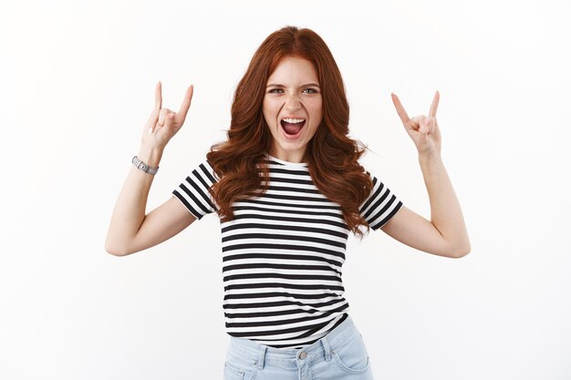 Wild and carefree good-looking redhead amused girl in striped t-shirt yelling excited, showing rock-n-roll, heavy metal gesture, open mouth enthusiastic and upbeat, enjoy awesome party