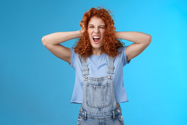 Wild daring rebellious cool stylish redhead curly girl having fun playful exciting mood touch hair yelling singing along awesome concert music enjoy positive summer vibes wear overalls.