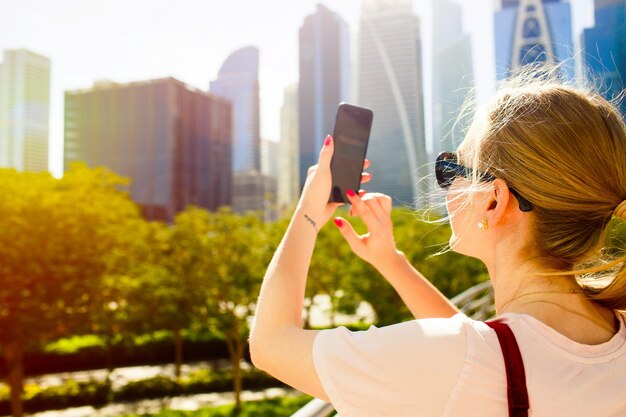 Wind blows woman's hair while she takes picture of beautiful skyscrapers on her smartphone