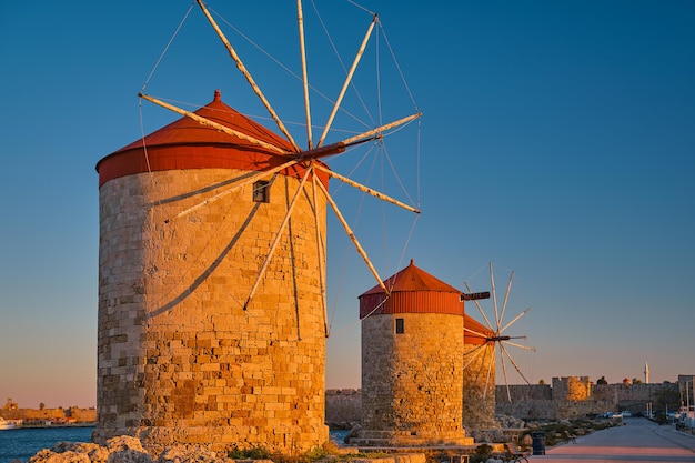 Mulini a vento sulla riva della baia durante il tramonto nella città di rodi sull'isola di rodi dell'isola dell'arcipelago del dodecaneso europavacanza e destinazione di viaggio popolare