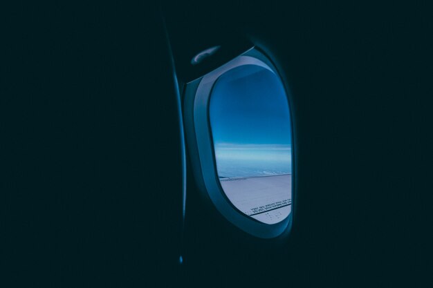 Window of the airplane with the view of the wing and blue sky