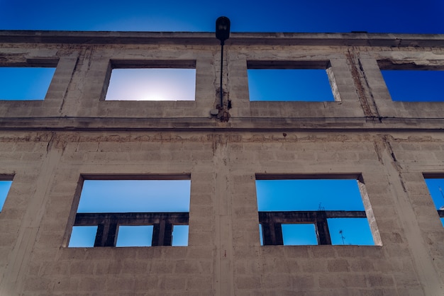 Окно заброшенного здания без отделки своей конструкции, интенсивного солнца и глубокого синего неба. Premium Фотографии