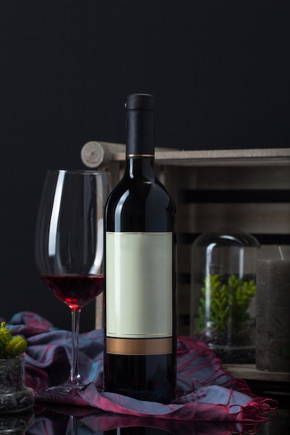 Бесплатное фото Бутылка вина с кубком, растением, шарфом, свечой и деревянной коробкой