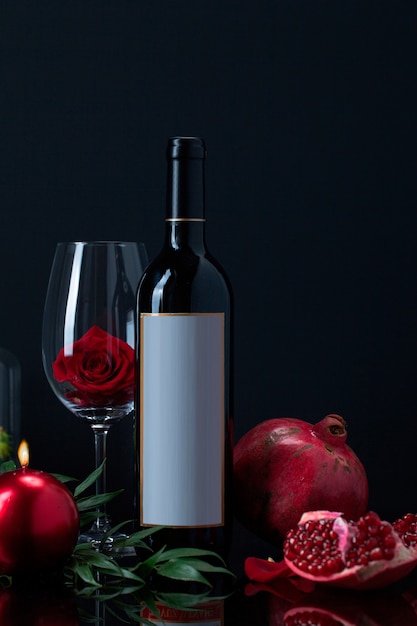 Free photo wine bottle with rose in goblet, candle, pomegranate and plant