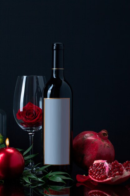 Wine bottle with rose in goblet, candle, pomegranate and plant