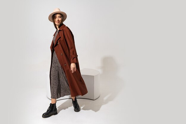 Модный образ Winer. Стильная брюнетка-модель в коричневом пальто и бежевой шляпе позирует