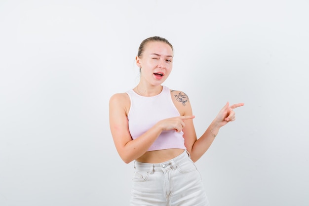 Winking girl is pointing at her right side on white background