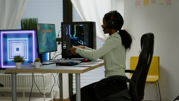 승자 흑인 게이머는 게임용 의자에 앉아 무선 컨트롤러로 공간 사수 비디오 게임을 하고 있습니다. RGB 강력한 개인용 컴퓨터에서 e스포츠 토너먼트를 위한 온라인 비디오 게임을 스트리밍하는 프로 사이버맨