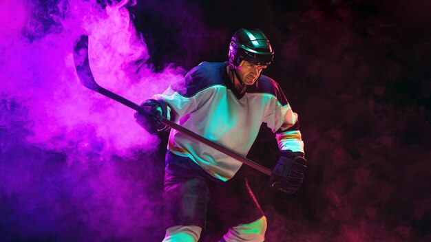 Winner. Male hockey player with the stick on ice court and dark neon colored wall. Sportsman wearing equipment, helmet practicing. Concept of sport, healthy lifestyle, motion, wellness, action.