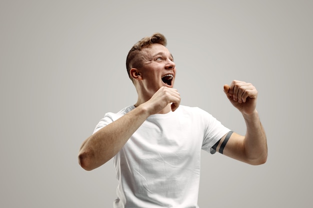 Winning success happy man celebrating being a winner. Dynamic image of caucasian male model on gray studio background. Victory, delight concept. Human facial emotions concept.