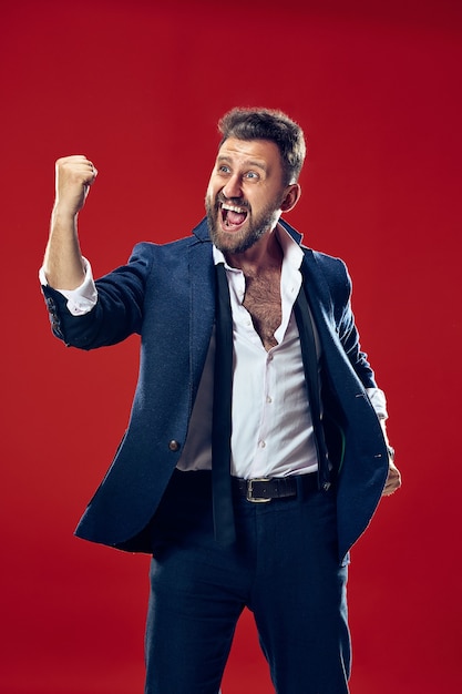 Winning success happy man celebrating being a winner. Dynamic image of caucasian male model on red studio background.