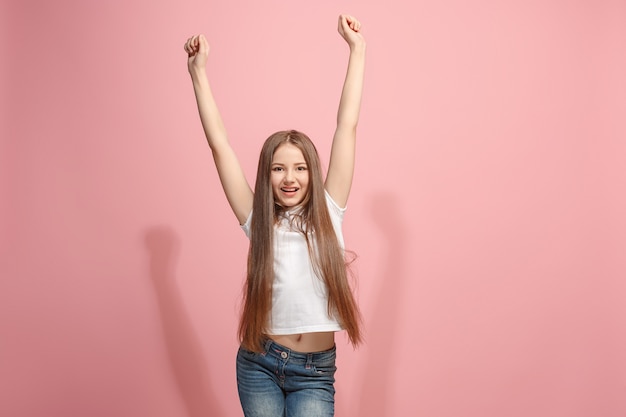 승리 성공 행복 한 십 대 소녀 승자가 되 고 축 하합니다. 핑크 스튜디오 벽에 백인 여성 모델의 동적 이미지. 승리, 기쁨 개념. 인간의 얼굴 감정 개념. 트렌디 한 색상
