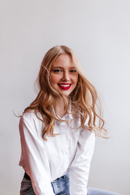 Winsome blonde girl in shirt with smile.  happy caucasian lady isolated on light wall.