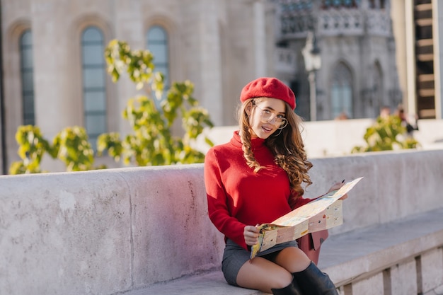 Winsome girl in short skirt sitting on stone bench with city map