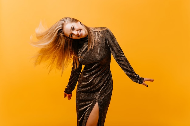 Winsome woman with blinde hair dancing in and laughing. Gorgeous woman in dress posing on orange.