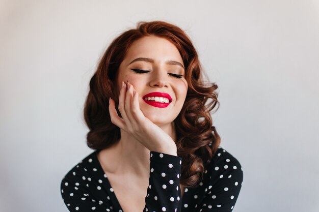 Winsome young lady laughing with closed eyes. Studio shot of appealing girl isolated on grey space.