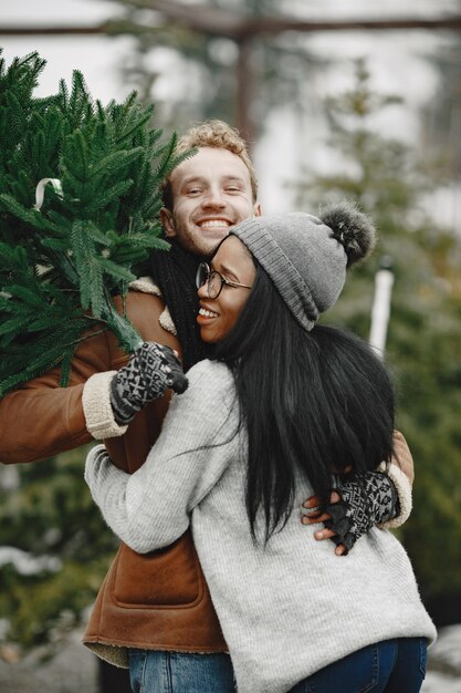 Winter concept. Guy in a brown coat. Salesman of Christmas Tree. International couple.