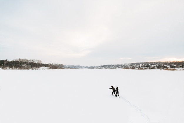 冬。男と女の子は冬の雪に覆われた凍った湖の上を移動します。