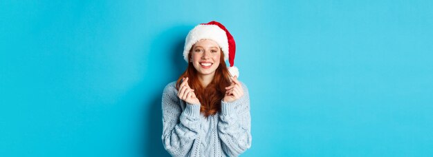 Бесплатное фото Зимние каникулы и концепция кануна рождества обнадеживающая рыжая девушка в новогодней шапке загадывает желание на рождество с