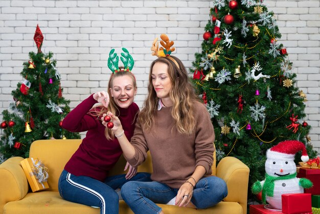 暖炉のそばで赤ワインのグラスとカップル セーターを着て クリスマスツリーの横にあるソファに座って頭にサンタの帽子をかぶった美しい白人の若い女性 プレミアム写真