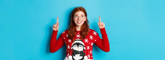 Free photo winter holidays and celebration concept cheerful teen girl with red hair looking dreamy at logo poin