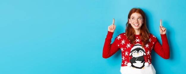 Free photo winter holidays and celebration concept cheerful teen girl with red hair looking dreamy at logo poin