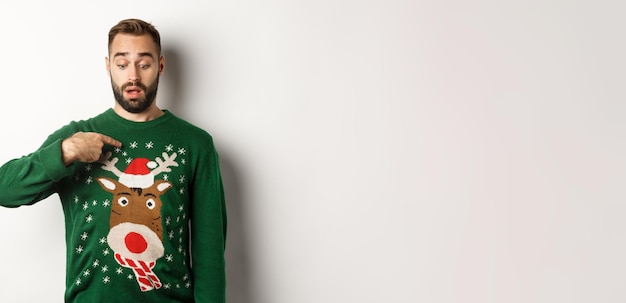 Free photo winter holidays and christmas confused guy in sweater pointing at himself standing puzzled over whit