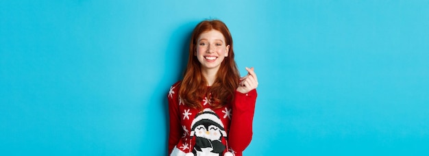 겨울 휴가 및 크리스마스 이브 개념 심장 si를 보여주는 크리스마스 스웨터에 귀여운 웃는 빨간 머리 소녀