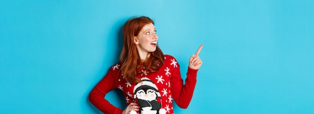 Free photo winter holidays and christmas eve concept happy and cute redhead girl in xmas sweater looking and po