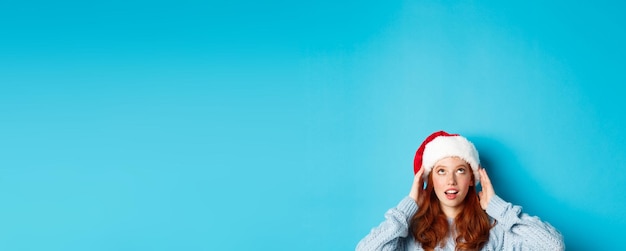 Free photo winter holidays and christmas eve concept head of cute redhead girl in santa hat appear from bottom