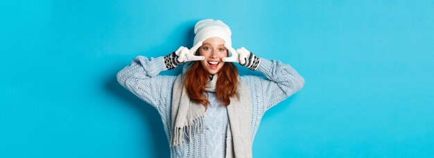 Winter and holidays concept cute redhead teen girl in beania gloves and sweater showing peace sign l