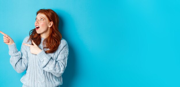 Winter holidays and people concept amazed redhead girl checking out promo offer pointing and looking