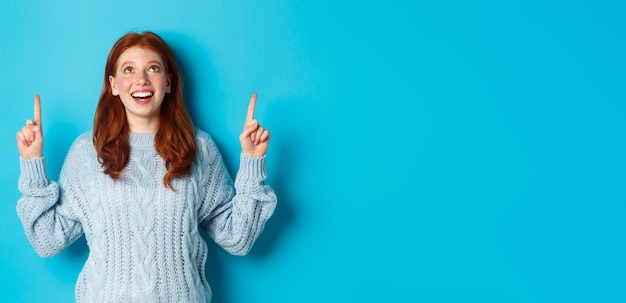 Free photo winter holidays and people concept beautiful teenage girl with red hair wearing sweater pointing fin