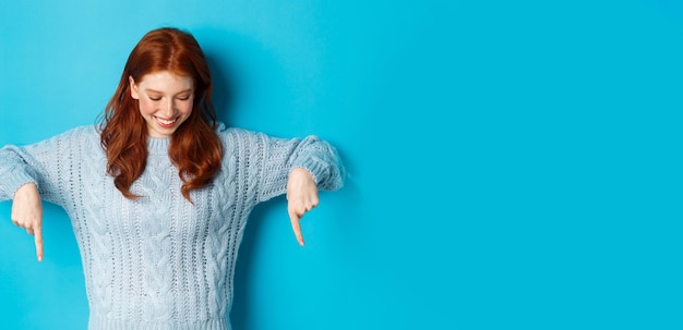 Vacanze invernali e concetto di persone ragazza rossa allegra in maglione che punta le dita verso il basso e guarda