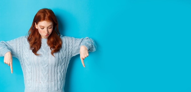 Winter holidays and people concept intrigued redhead girl pointing and looking down thoughtful makin