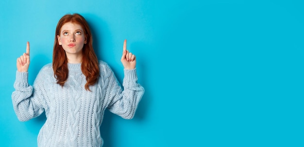 Free photo winter holidays and people concept thoughtful redhead girl in sweater staring and pointing fingers u